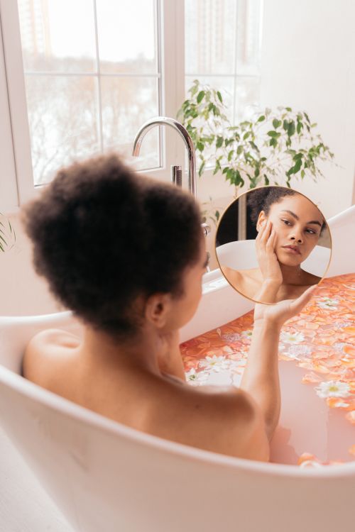 Free Woman in a floral bath holds a mirror, reflecting her self-care and skin routine. Stock Photo