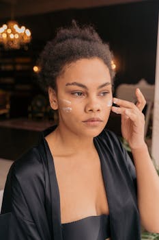 Close-up of a young woman applying face cream indoors, focusing on skincare and beauty routine.