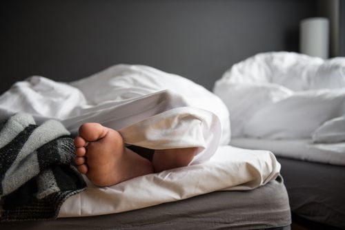 Free A close-up of a bare foot poking out from under a soft duvet in a modern bedroom. Stock Photo