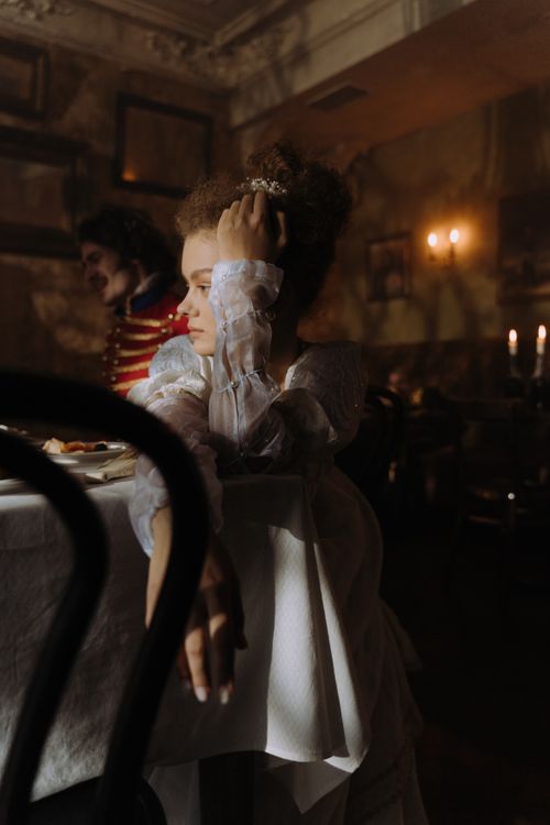 Free A thoughtful woman in period costume sits in a dimly lit room, capturing a vintage atmosphere with candlelight. Stock Photo