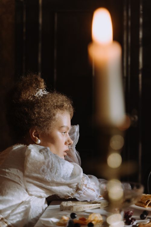 Free A woman in period costume sitting thoughtfully by a candlelit table. Stock Photo