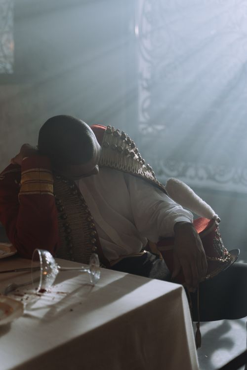 Free A man in historical costume sits slumped over a table, illuminated by soft morning light. Stock Photo