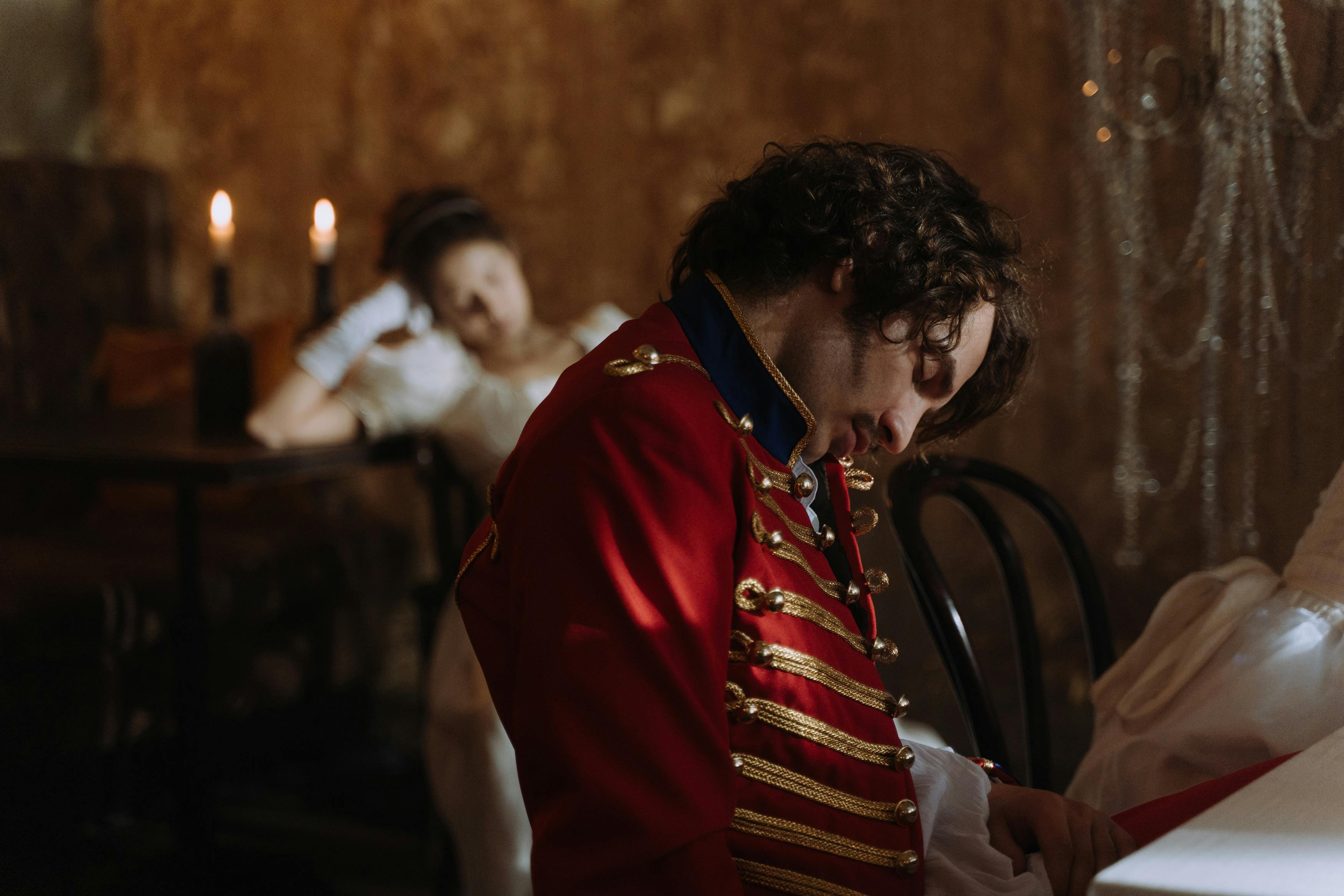 Free Guests in period costumes asleep after a themed ball setting, vibrant scarlet tunic worn by one. Stock Photo
