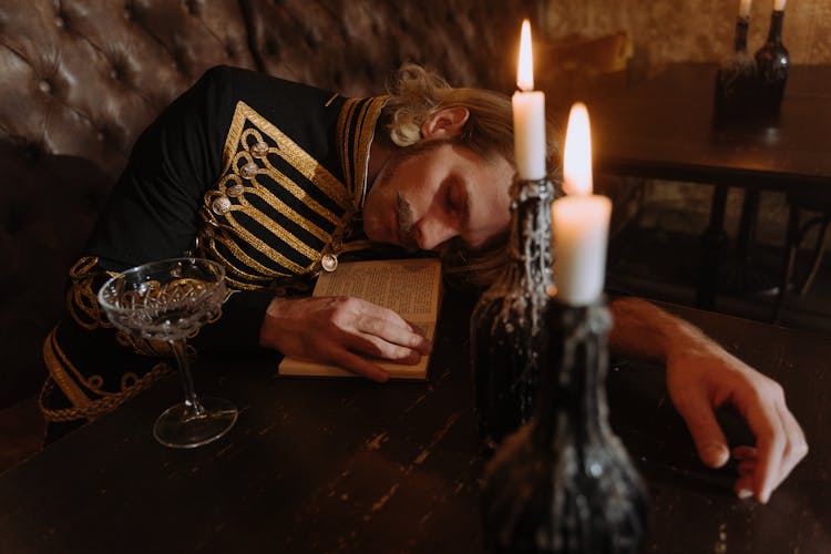 Man In Uniform Sleeping On Book Under Candlelight