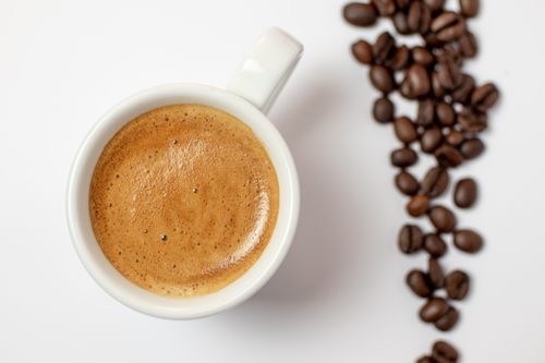Free A warm cup of espresso with rich foam, served alongside scattered roasted coffee beans. Stock Photo