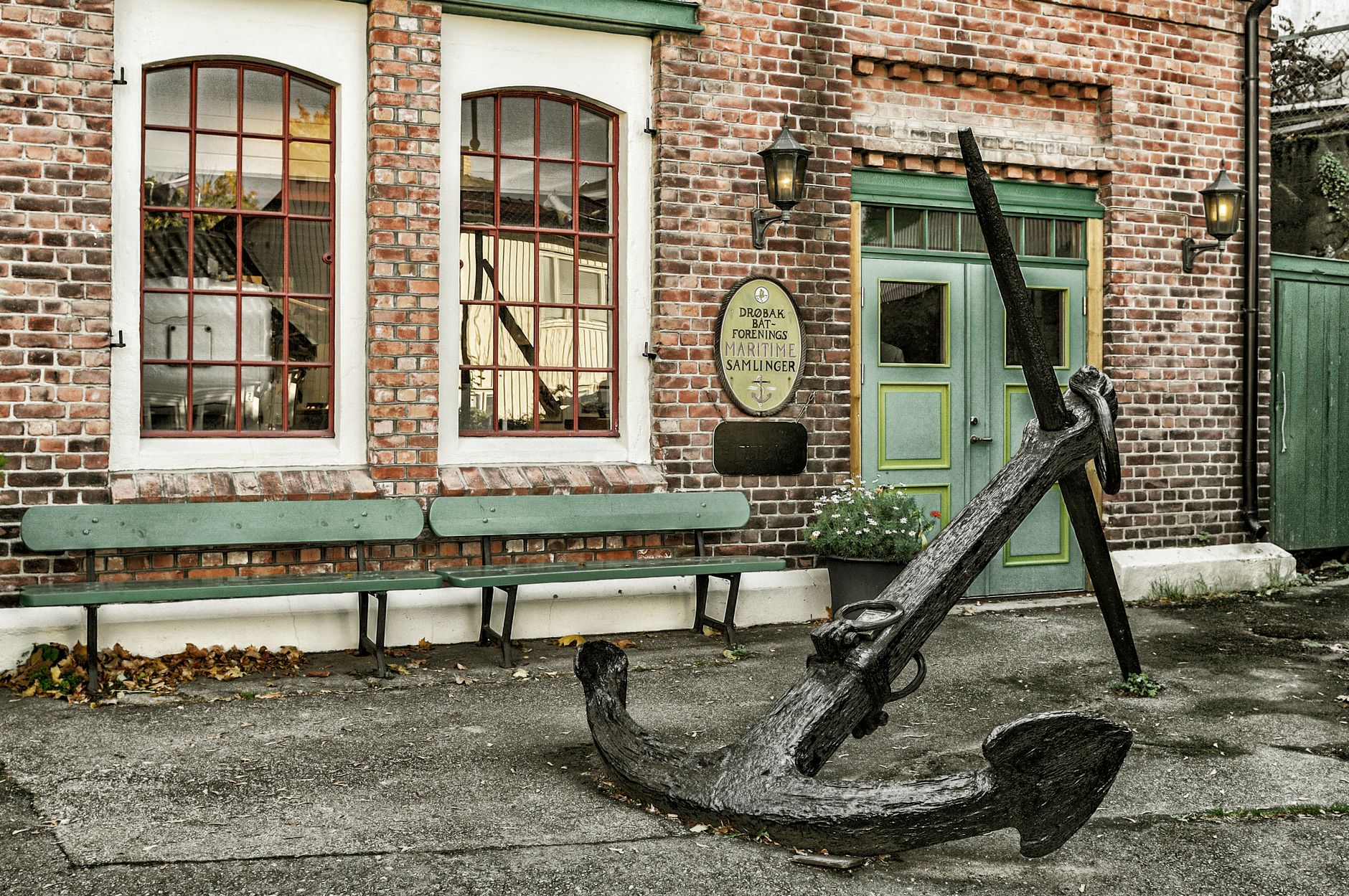 Old brick building with antique anchor outside, showcasing maritime history in urban setting.