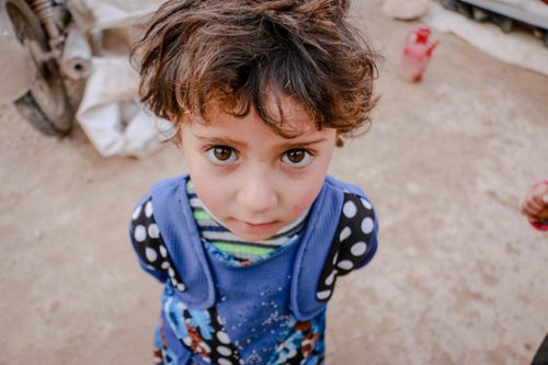 Free From above of crop little girl looking at camera on blurred background of rustic yard in daytime Stock Photo