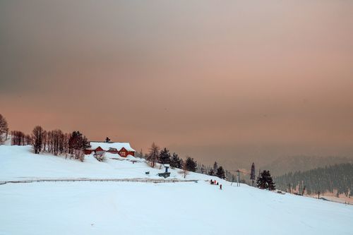 Free Capture of a serene winter landscape with snow-covered hills and a house at sunset in Gulmarg. Stock Photo
