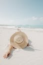 阳光明媚的夏日，戴着草帽的匿名女性旅行者在热带度假胜地平静的大海附近的沙滩上放松身心