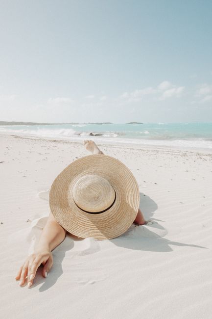 Anonymous female traveler in straw sunhat relaxing on sandy shore near calm sea in tropical resort on sunny summer day