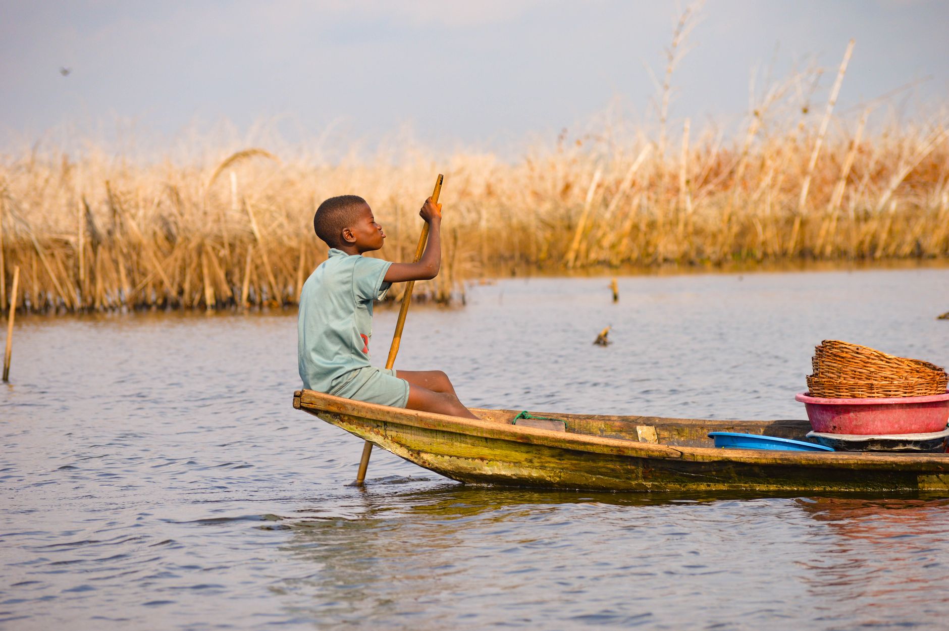 A young boy paddles a canoe in the serene waters of Ganvié, Benin, showcasing traditional fishing methods.