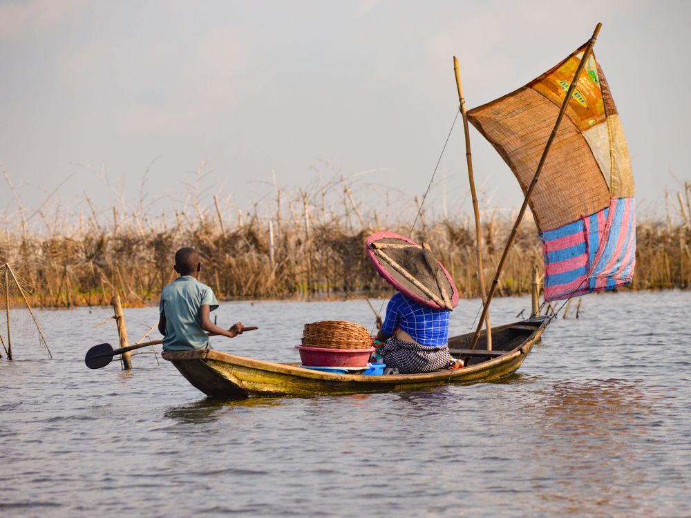 Boy and woman in hat in wooden sail boat, Benin