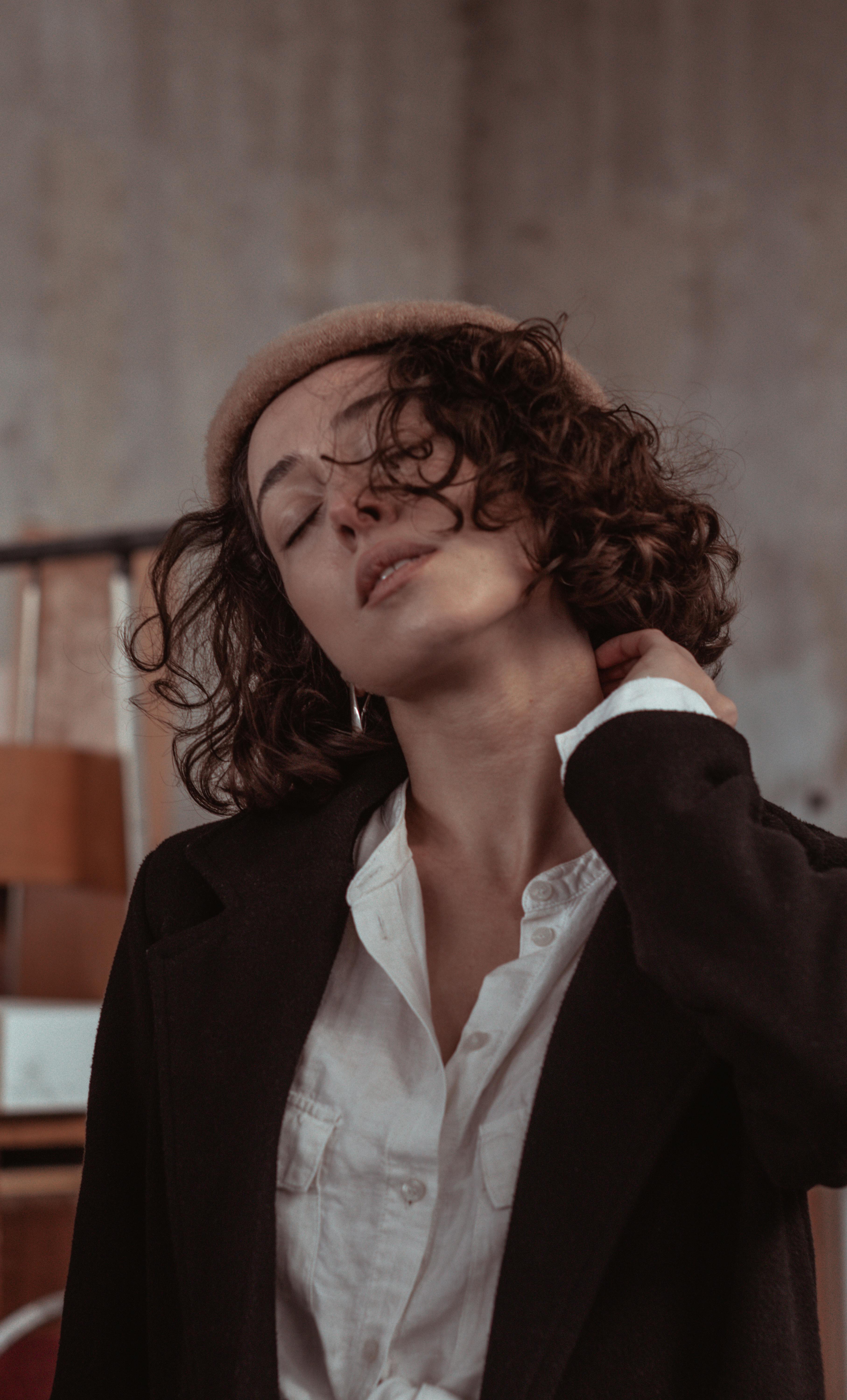 Fashionable woman with curly hair posing indoors in classic attire, exuding elegance.