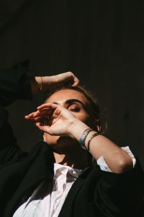 Free Chic woman in black suit shields her eyes from the sun, showcasing fashion and elegance. Stock Photo