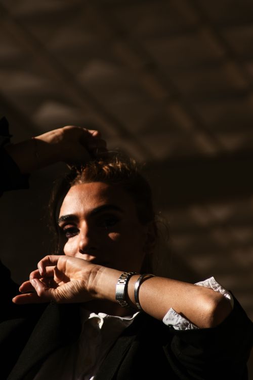 Free A young woman posing with hand on head, captured in dramatic lighting creating a moody atmosphere. Stock Photo