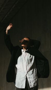 Fashionable woman in a black suit and white shirt posing artistically with her arm raised against a dark background.