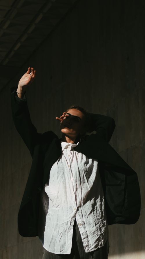 Free Fashionable woman in a black suit and white shirt posing artistically with her arm raised against a dark background. Stock Photo