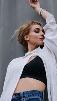 Young woman with arm raised posing against a concrete wall in a fashion photoshoot.