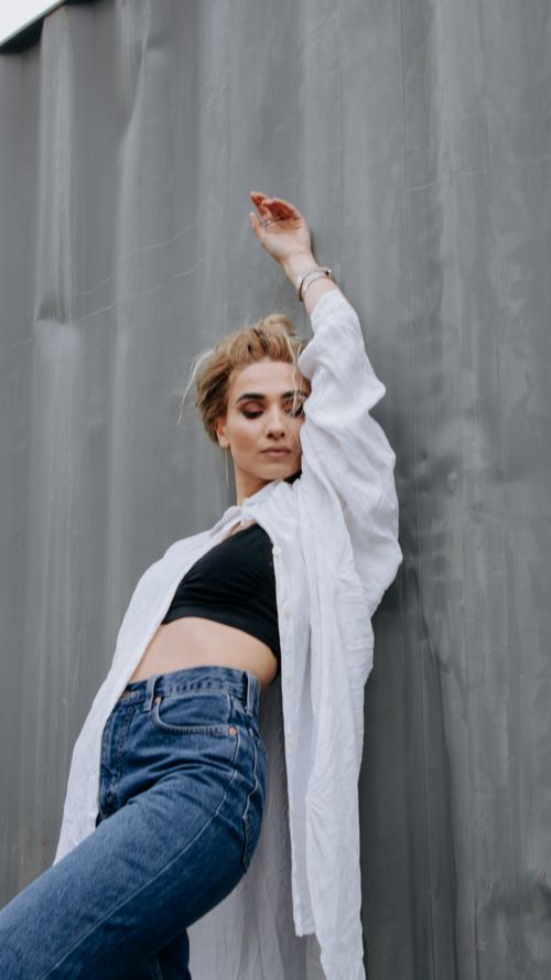 Free Young woman with blonde hair posing confidently in casual fashion against a gray wall. Stock Photo