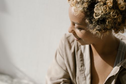 Free A woman with curly hair is smiling softly indoors in natural light. Stock Photo