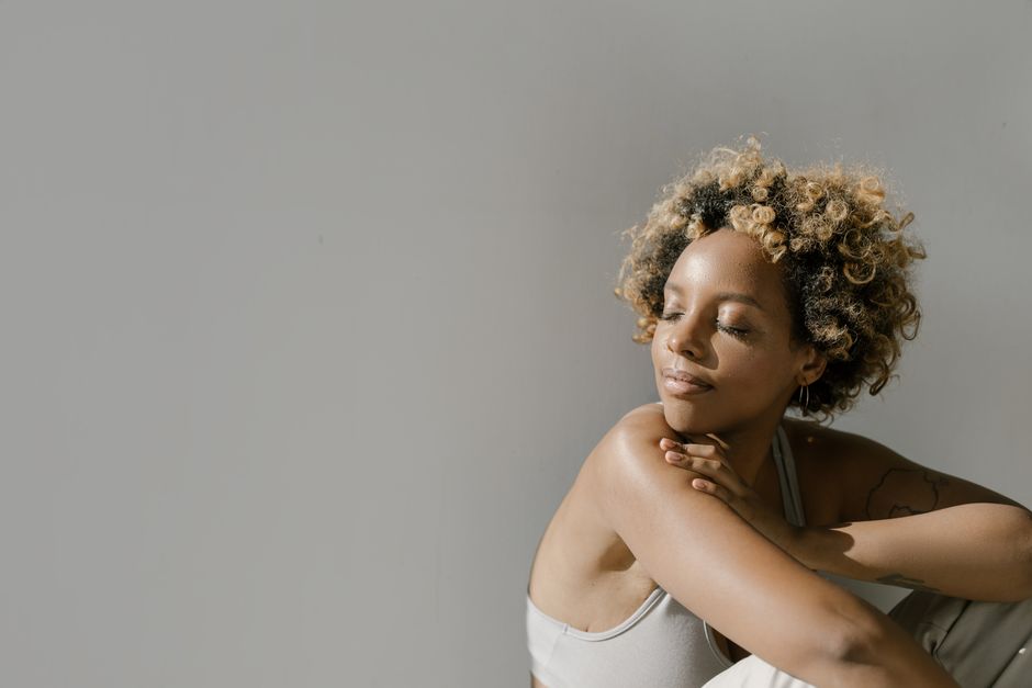 A serene young woman enjoys sunlight indoors, embracing a moment of calm.