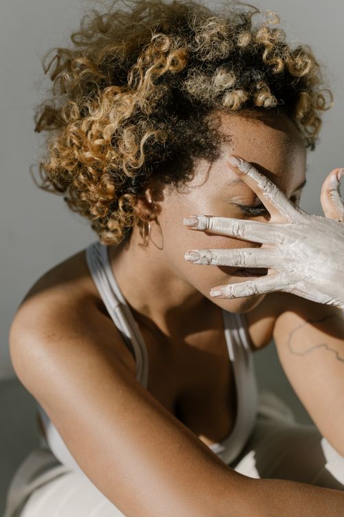 Free A woman with curly hair obscures her face with a painted hand in soft daylight. Stock Photo