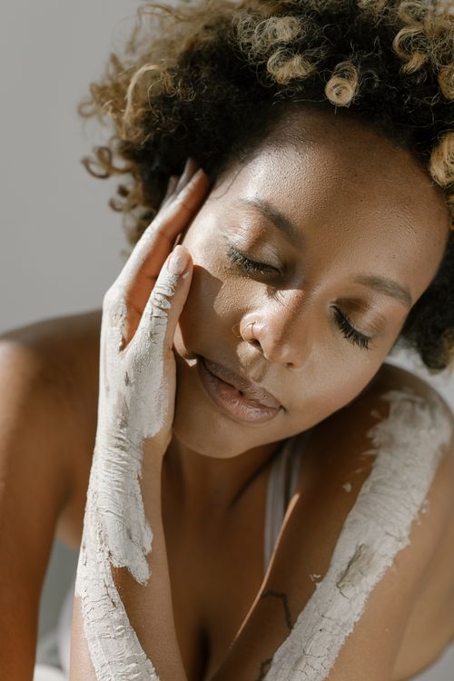 Free Portrait of a woman with closed eyes, clay-covered skin, and afro hair indoors. Stock Photo