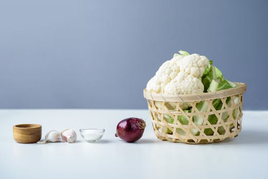 Fresh cauliflower with garlic and onion displayed in a wicker basket on a studio background.