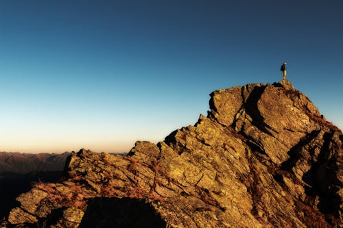 бесплатная Человек, стоящий на вершине скалы днем Стоковое фото