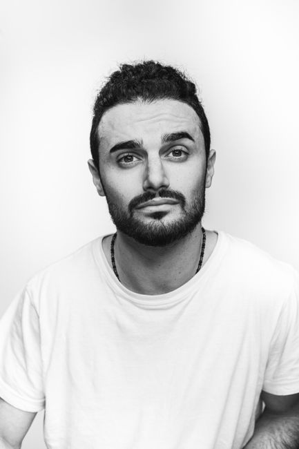 Monochrome portrait of a bearded man in a white shirt, looking at the camera.