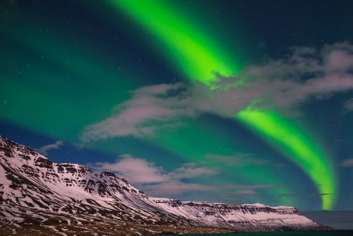 Free A mesmerizing display of the Aurora Borealis above a snowy mountain range under a starry night sky. Stock Photo