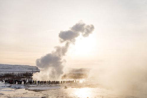Free Crowds gather to witness a geyser eruption amidst the snowy Icelandic landscape. Stock Photo