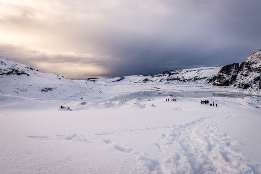 Explore a vast snowy landscape with distant hikers in a winter wonderland under a dramatic sky.