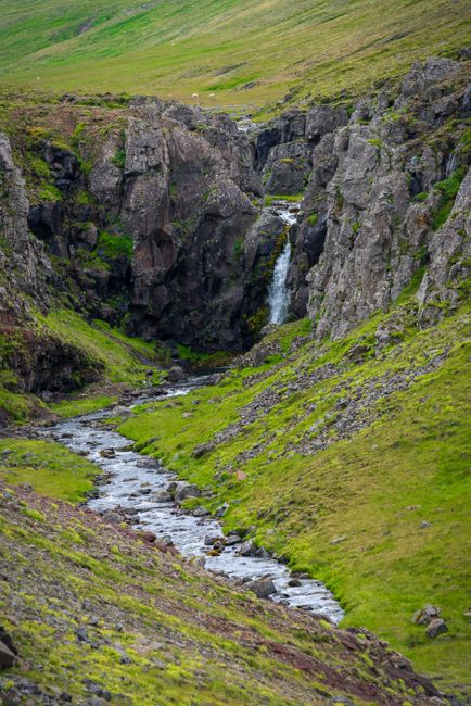 A picturesque waterfall flowing through a lush green valley, surrounded by rocks.
