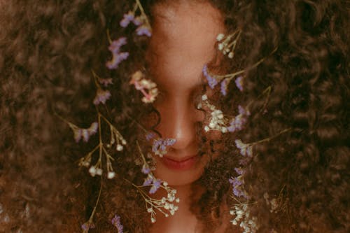 Free Headshot of anonymous content female with small bright flowers with white and purple petals tangled in brown hair covering face Stock Photo