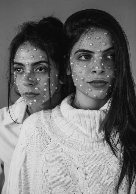 Black and white of serious young women with long hair and stylish pearl beads on face looking away while standing in room