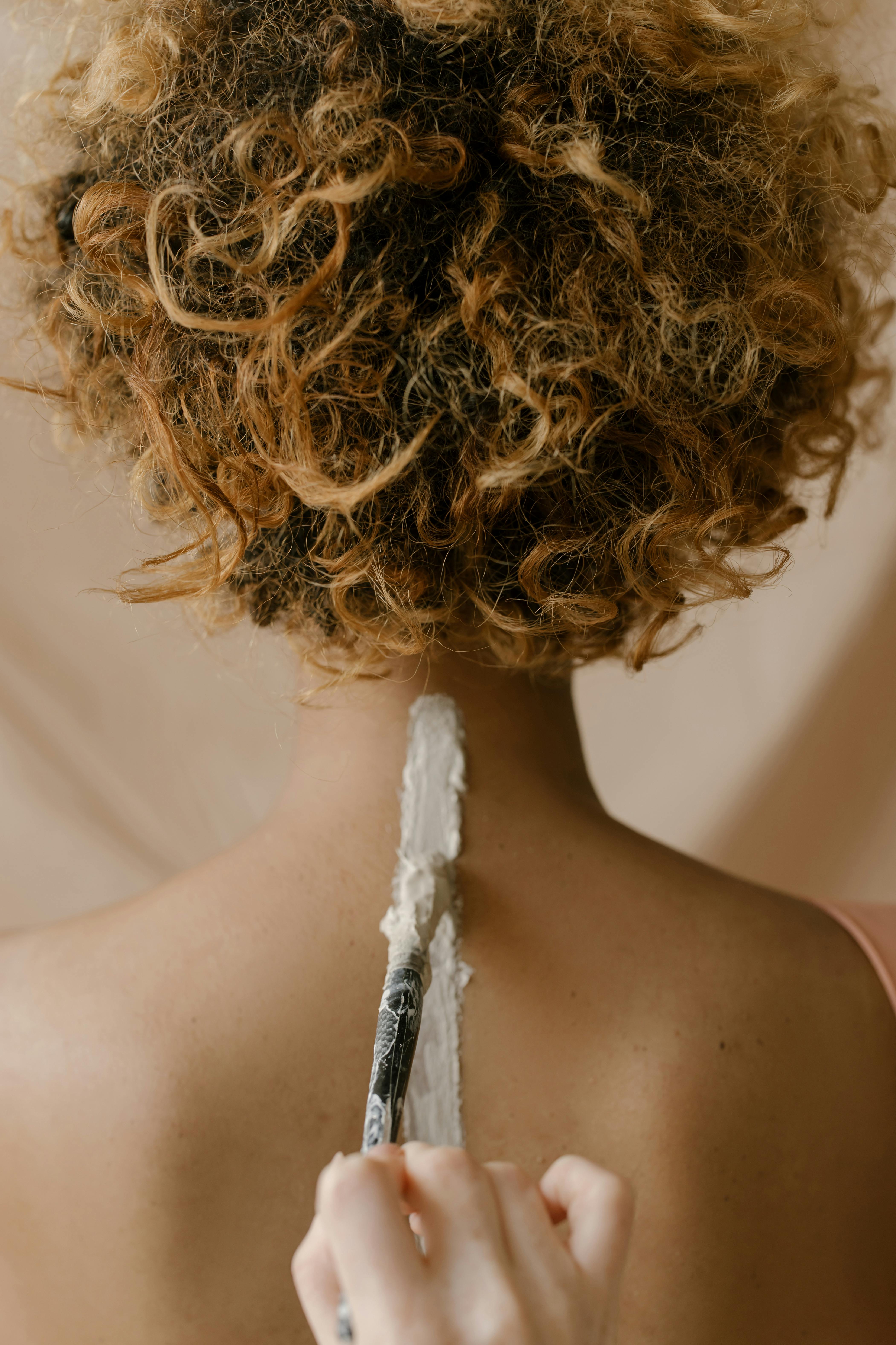 Close-up of a hand applying clay paint to a woman's back, showcasing creative artistry.