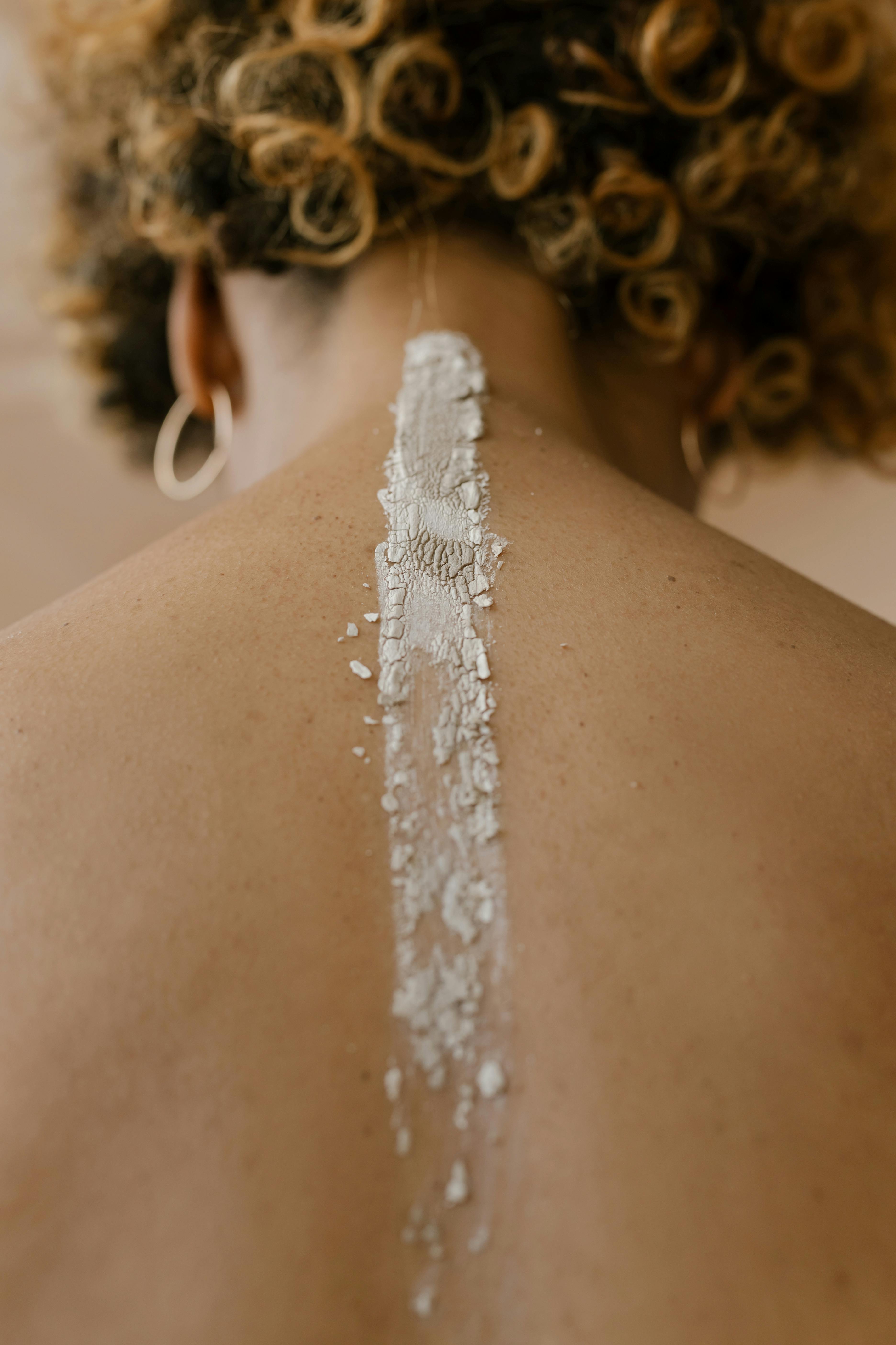 Artistic close-up of a woman's back with a decorative line of clay, emphasizing texture and creativity.