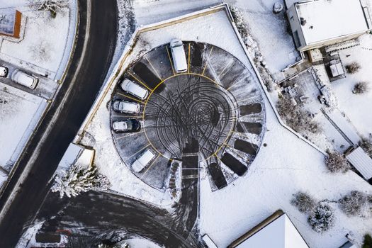 Snowy aerial view of circular parking lot with cars in Orbe, Switzerland
