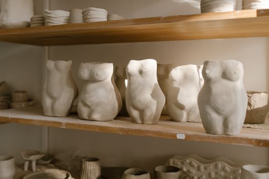 Ceramic sculptures of torsos on a wooden shelf, creating an artistic and creative display in a pottery studio.