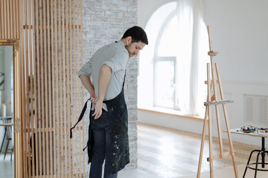 Creative man putting on apron in a bright studio with art supplies and easel, preparing to paint.