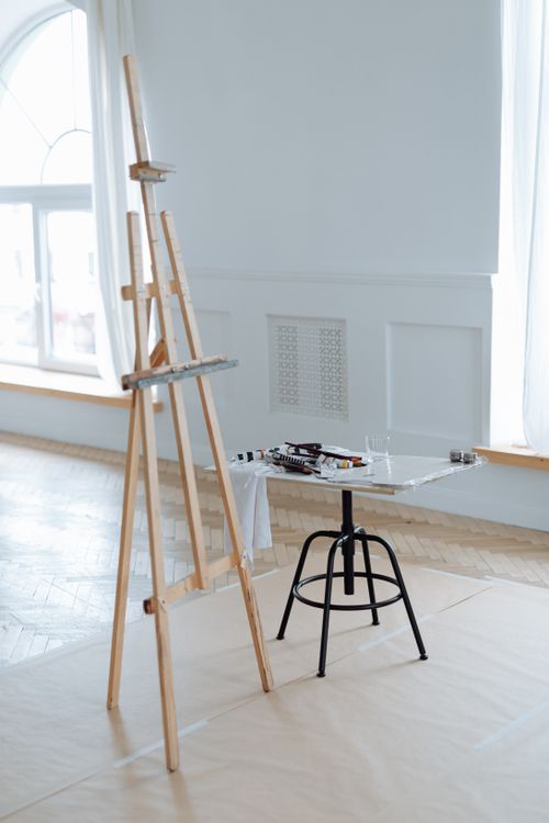 Free Bright art studio featuring a wooden easel and painting supplies on a glass table. Stock Photo