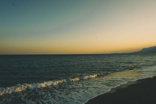 A tranquil view of the Antalya coast at sunset with gentle waves on the shore.