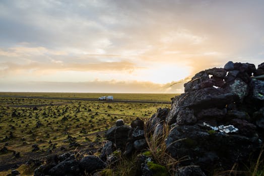 Beautiful sunset view over a vast countryside landscape with a road and distant vehicle, highlighting natural beauty.
