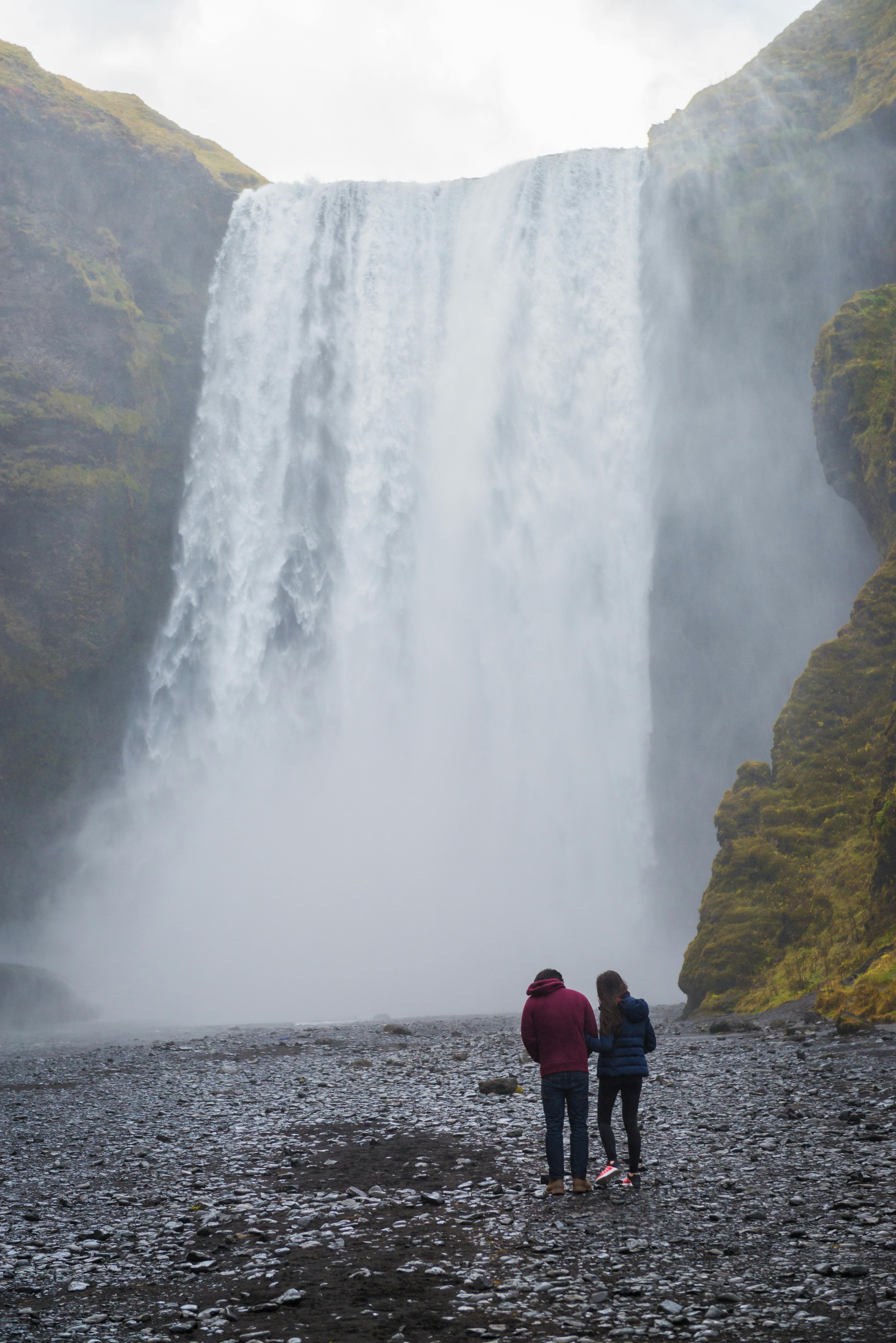 Back view of a couple standing in awe of a stunning waterfall cascade in nature.