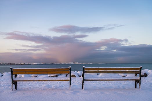 Captivating winter scene of snow-covered benches overlooking a serene sea and cloudy sky.