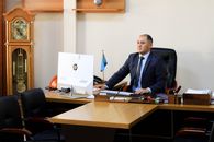 A serious businessman in a black suit focuses on work at his office desk with a computer and office decor.