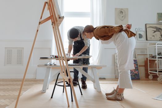 Two artists collaborating on a painting in a light-filled studio.