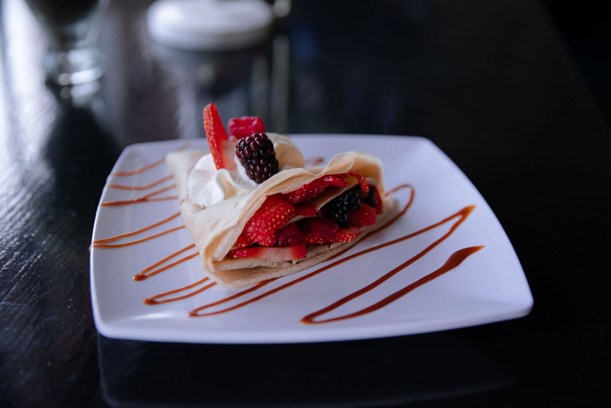 Folded crepe filled with strawberries and blackberries, whipped cream, caramel sauce stripes on square plate