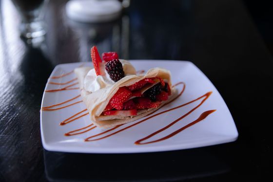Folded crepe filled with strawberries and blackberries, whipped cream, caramel sauce stripes on square plate